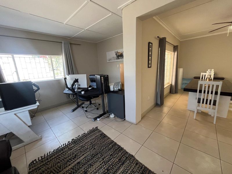 Open plan living area featuring tiled flooring and security bars on windows, connecting a workspace to a dining area.