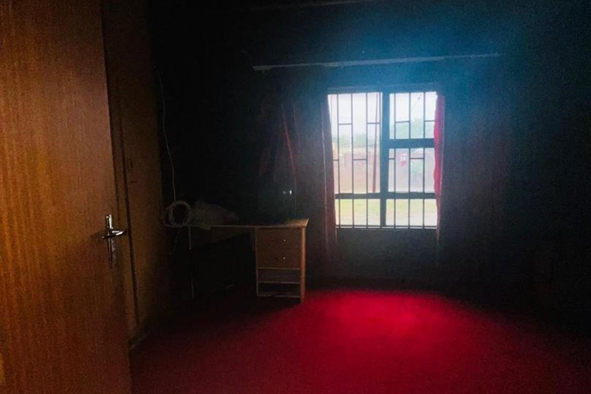 A dimly lit bedroom featuring wood-paneled walls, red carpeting, and a window with security bars.