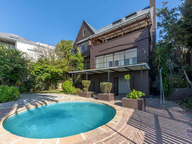 Rear exterior view of a multi-story house featuring a swimming pool, paved patio area, and a balcony with metal railings.