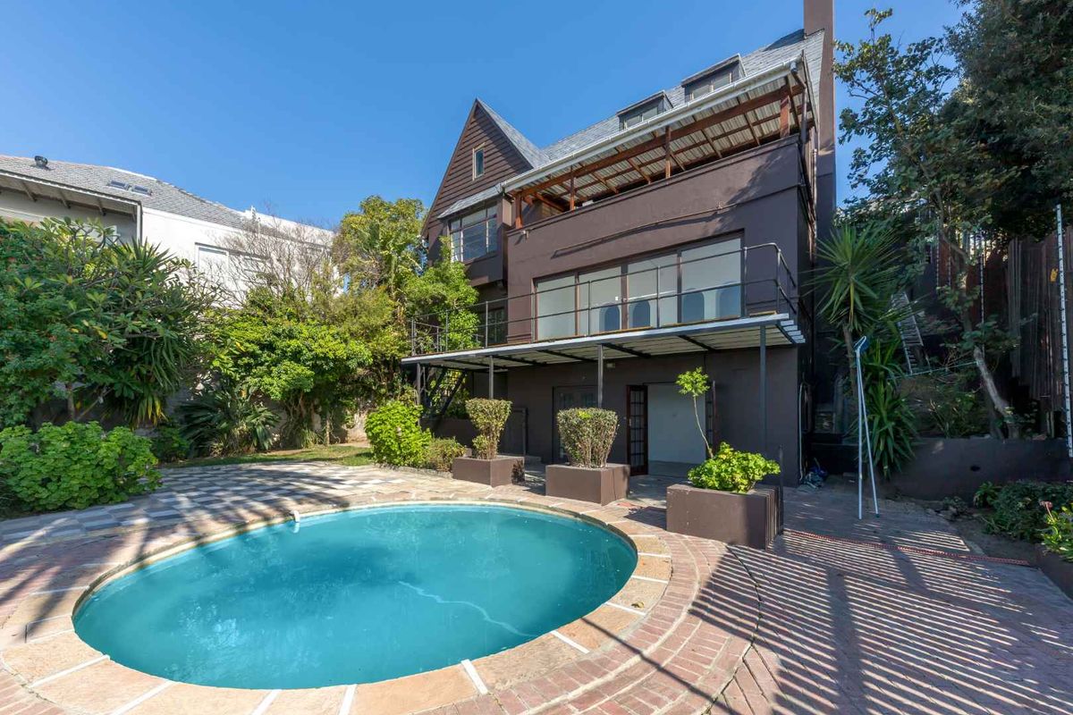 Rear exterior view of a multi-story house featuring a swimming pool, paved patio area, and a balcony with metal railings.