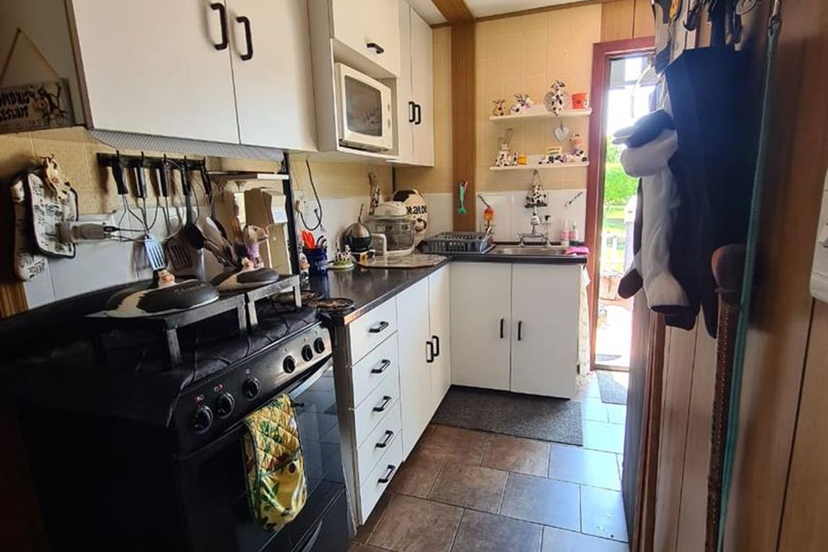 Compact kitchen featuring white cabinetry, dark countertops, a freestanding oven, and tiled flooring with direct access to the rear exterior.