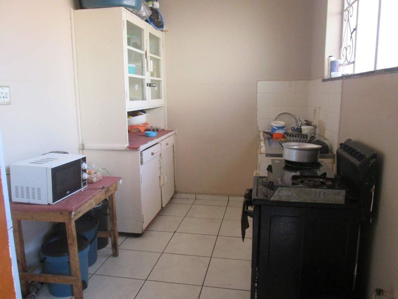 A functional kitchen space featuring tiled flooring, built-in cabinetry, and a tiled splashback, offering potential for modernization and cosmetic updates.