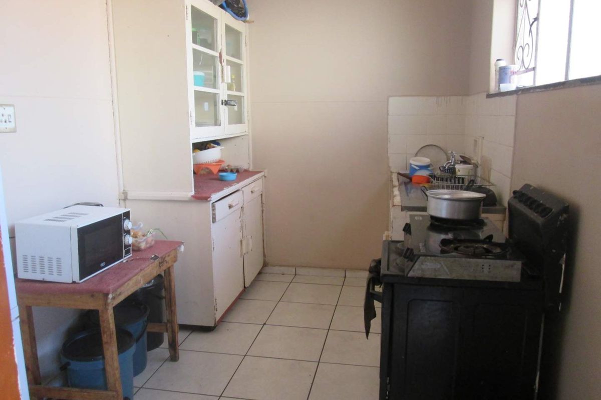 A functional kitchen space featuring tiled flooring, built-in cabinetry, and a tiled splashback, offering potential for modernization and cosmetic updates.