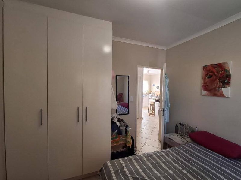 A bedroom featuring a large built-in wardrobe, neutral wall finishes, and tiled flooring, with a view through to the adjacent living area.