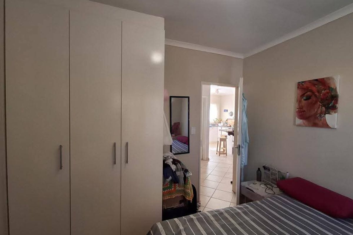 A bedroom featuring a large built-in wardrobe, neutral wall finishes, and tiled flooring, with a view through to the adjacent living area.