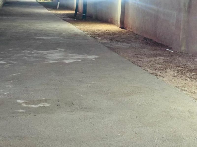A concrete driveway at dusk featuring perimeter walling and installed exterior lighting fixtures.