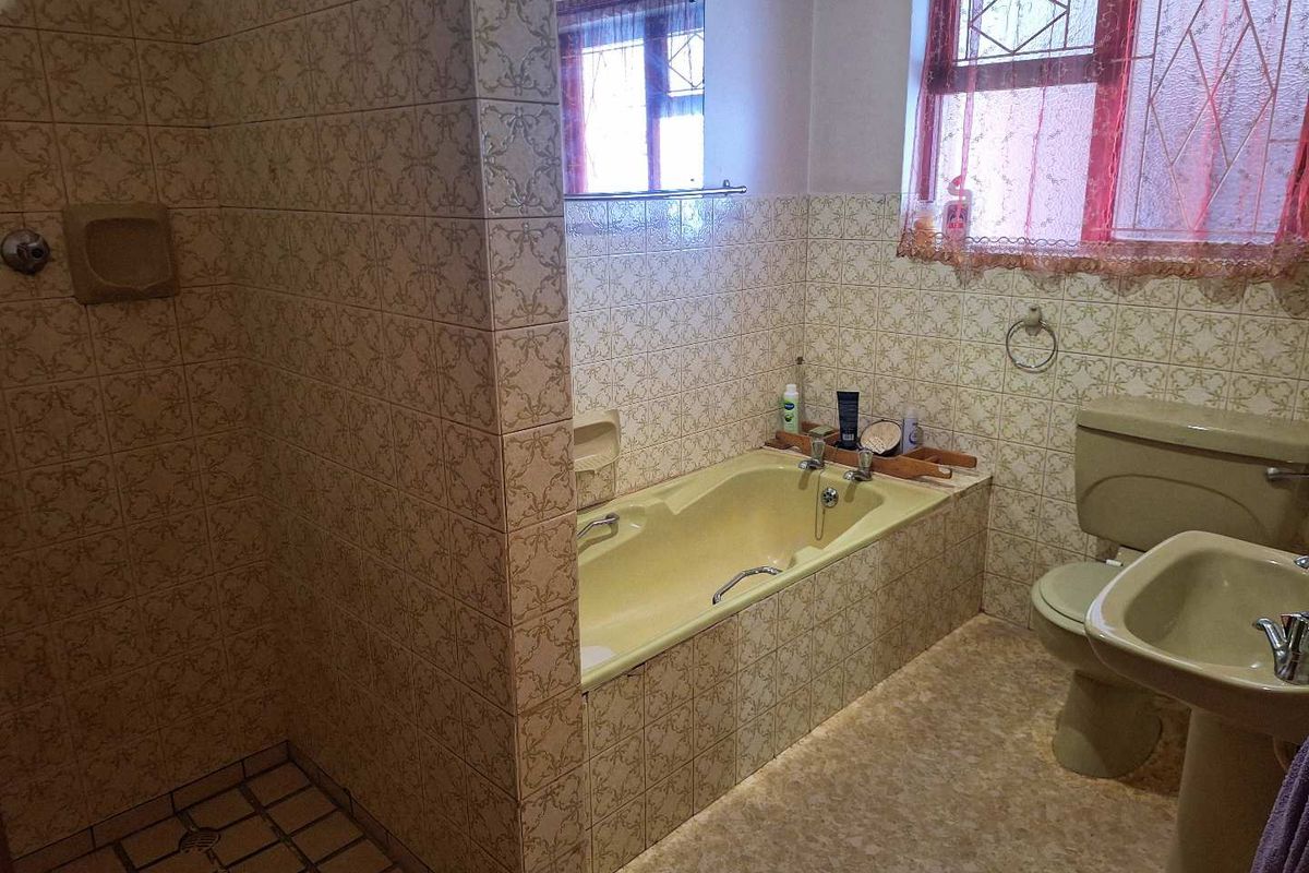 A dated bathroom featuring a built-in bathtub, pedestal sink, toilet, and a separate tiled shower enclosure with patterned wall tiles.