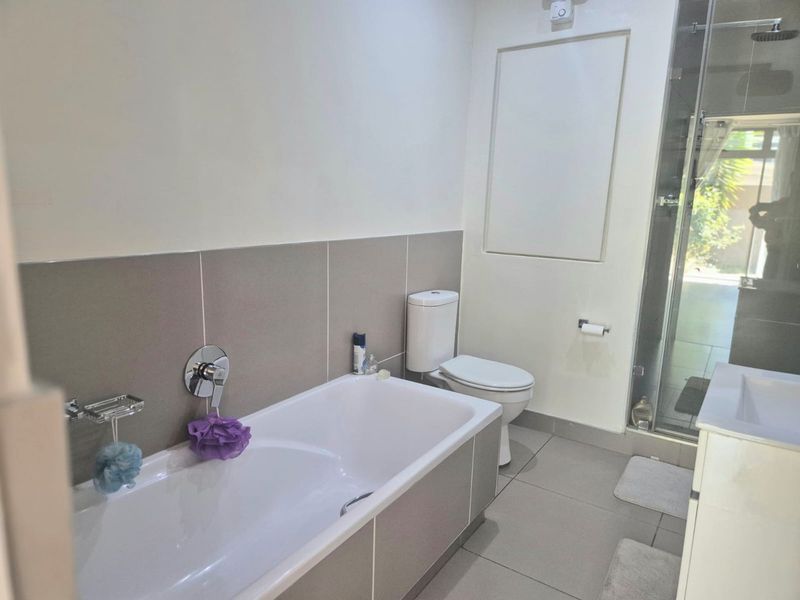 A modern bathroom featuring a bathtub, a separate shower enclosure, a toilet, and a vanity unit with neutral wall and floor tiling.