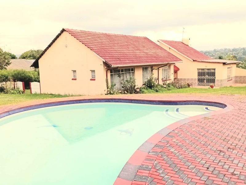 A residential property featuring a swimming pool with a paved surround, set against the rear elevation of the house with a pitched roof.