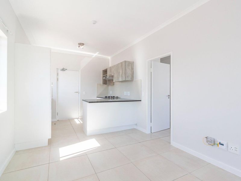 A bright, open-plan living and kitchen area featuring neutral tiled flooring, modern cabinetry, and a built-in gas hob.