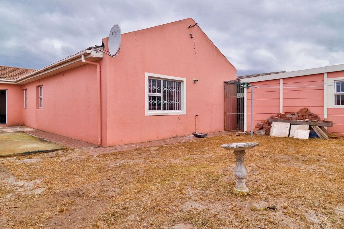 Rear view of the property featuring a pink exterior facade, security bars on windows, and a paved patio area leading to a garden.
