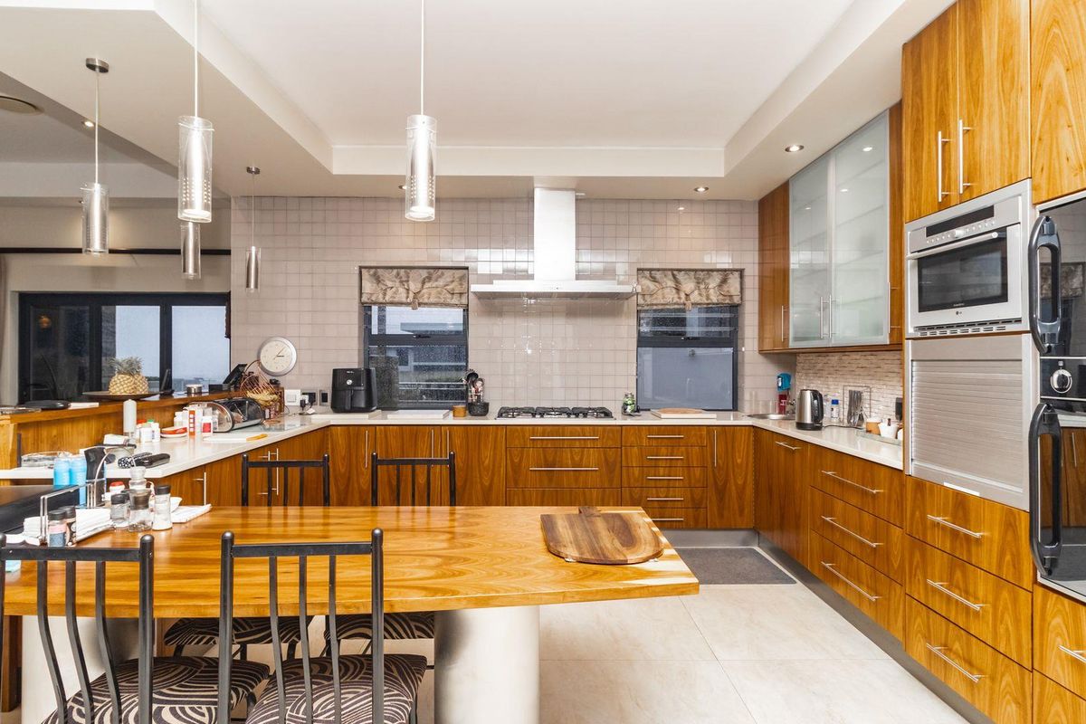 Spacious kitchen featuring warm wood cabinetry, integrated stainless steel appliances, a gas hob, extractor fan, and a large breakfast bar island.