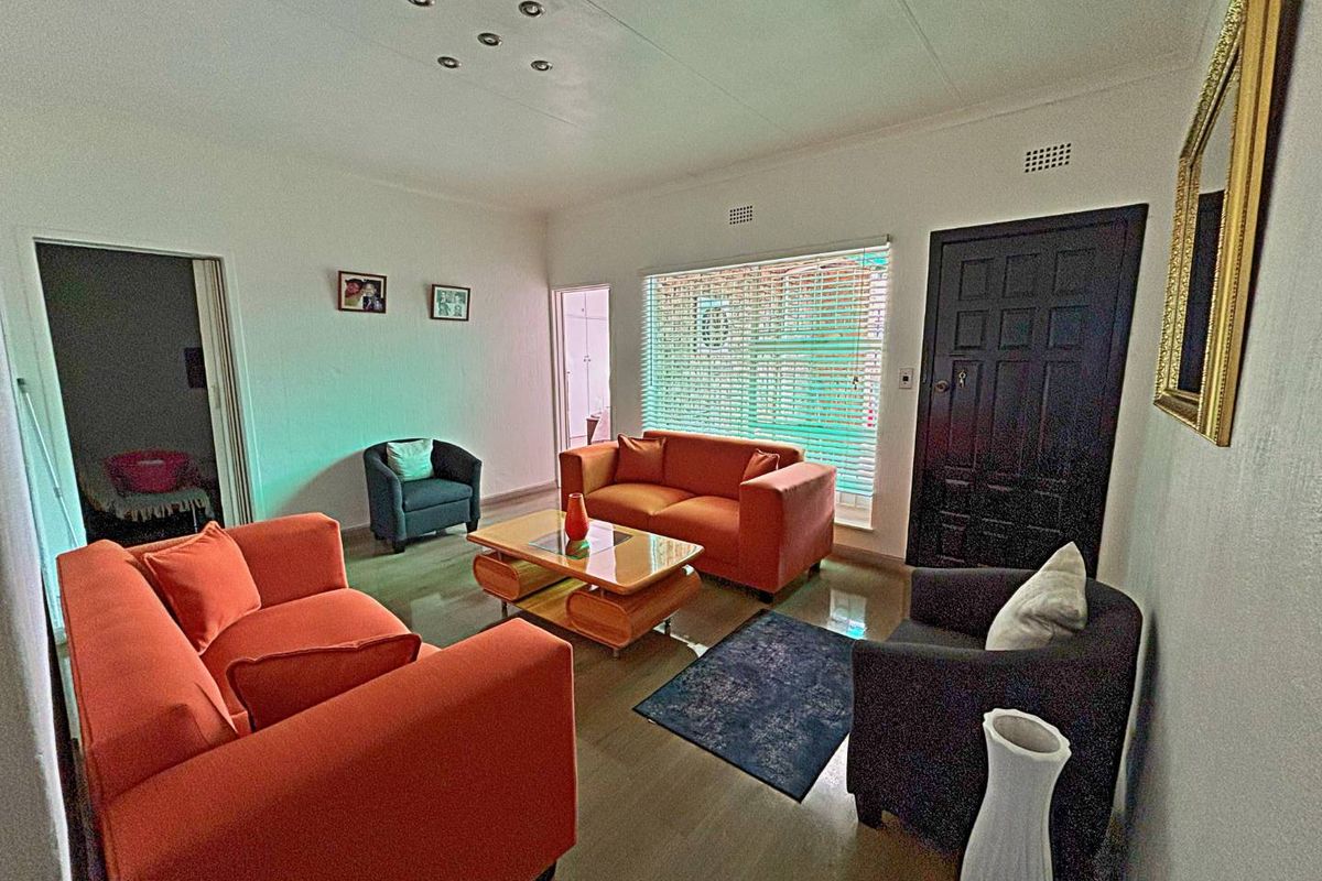 A bright living room featuring tiled flooring, recessed ceiling lighting, and a dark panelled entrance door with window blinds.