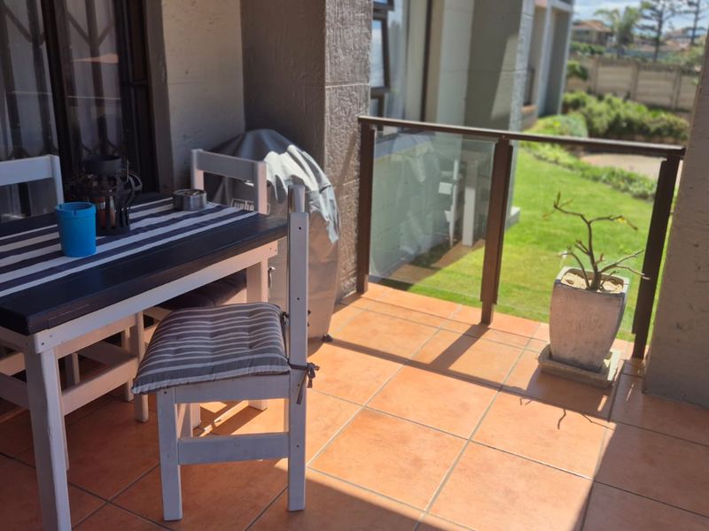A covered balcony featuring tiled flooring and a modern glass balustrade, offering a pleasant outdoor space for relaxation.