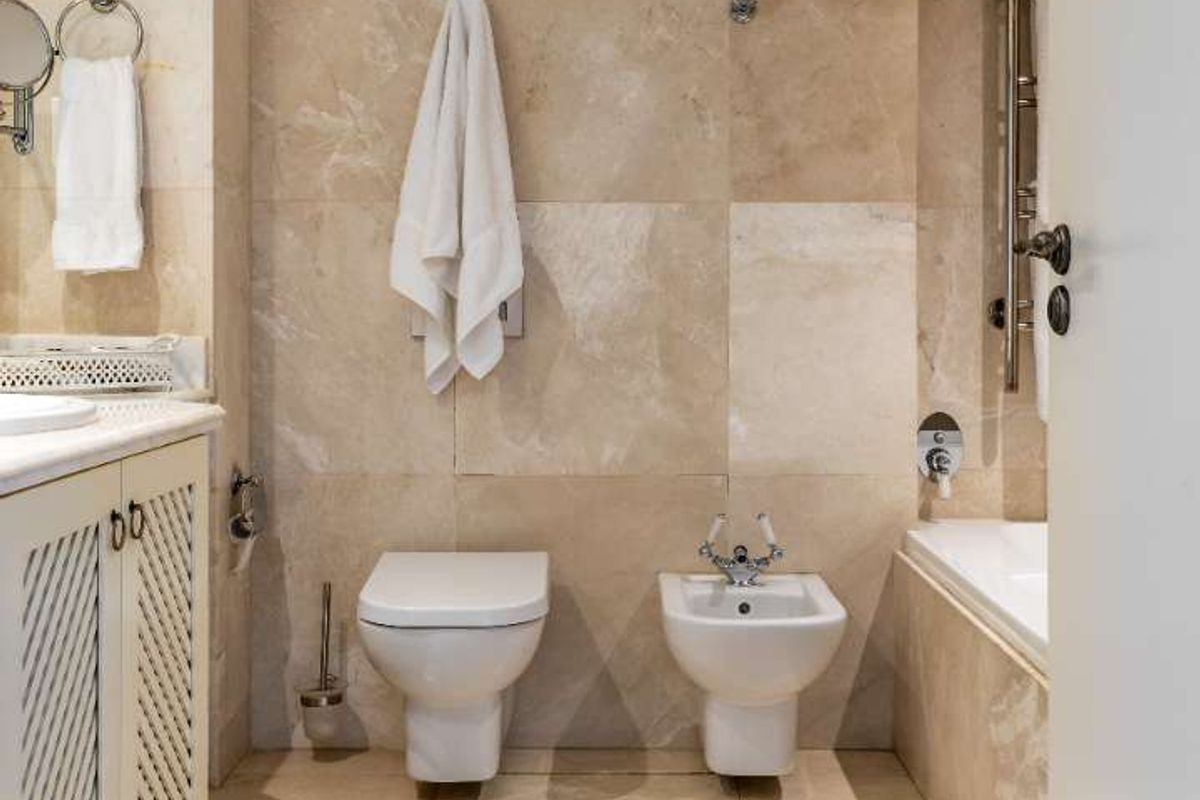 A well-maintained bathroom featuring stone wall and floor tiles, a wall-mounted toilet, bidet, bathtub, and a vanity cabinet with a heated towel rail.