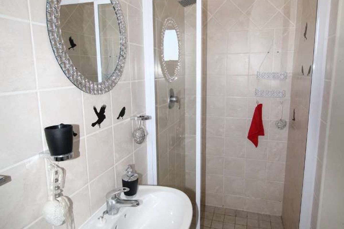 A functional bathroom featuring a wall-mounted basin, mixer tap, and a tiled shower enclosure with a glass door.