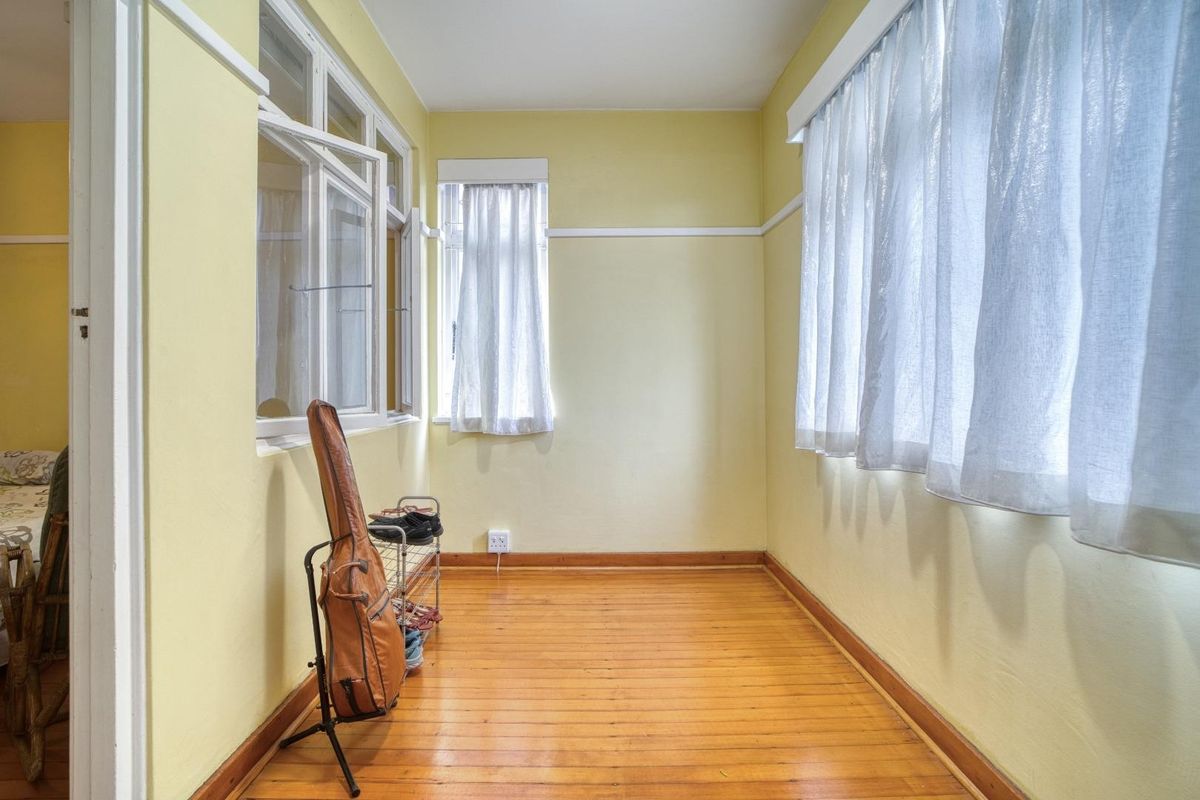 A bright, empty bedroom featuring original timber flooring, picture rails, and large windows that provide ample natural light.