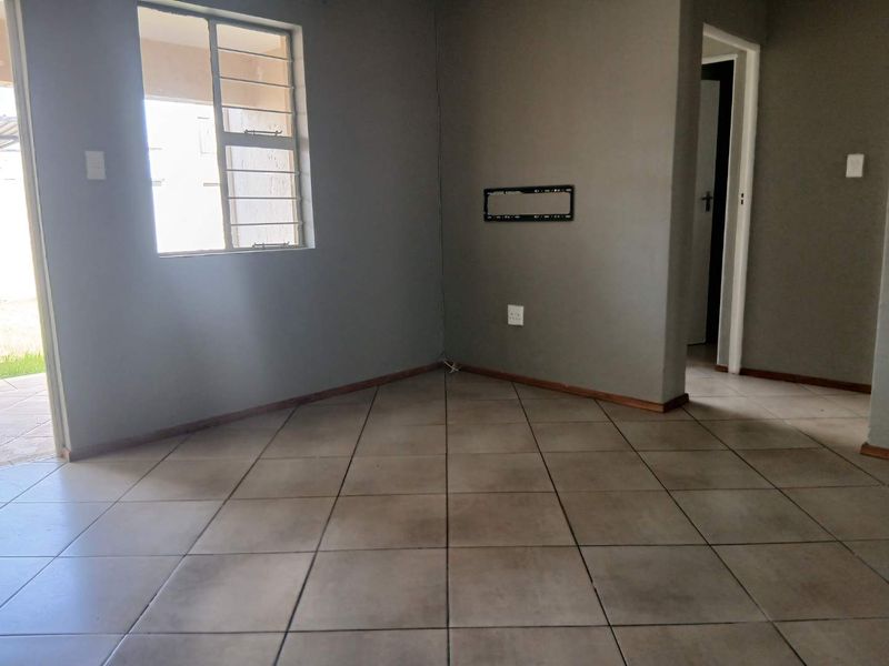 An empty living room featuring tiled flooring, grey painted walls, and a wall-mounted television bracket, providing a blank canvas for interior design.