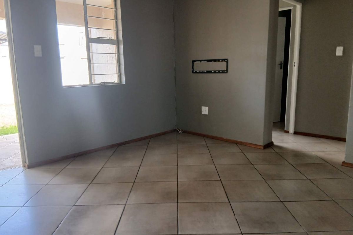 An empty living room featuring tiled flooring, grey painted walls, and a wall-mounted television bracket, providing a blank canvas for interior design.