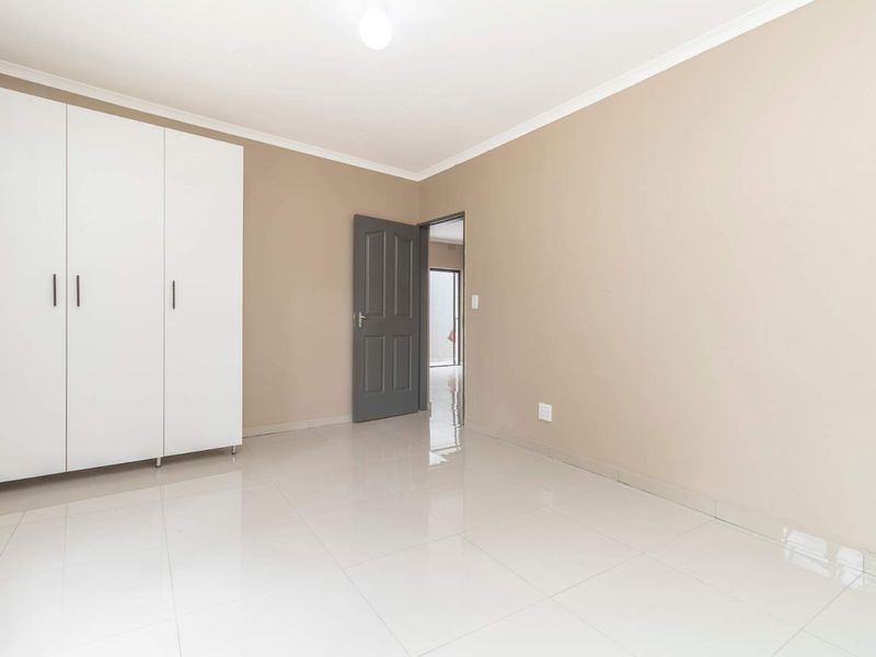 A clean, empty bedroom featuring neutral wall tones, white tiled flooring, and a built-in wardrobe, offering a blank canvas for personalization.