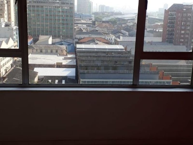 An interior view looking out through a large window, showcasing an expansive urban cityscape and surrounding building architecture.