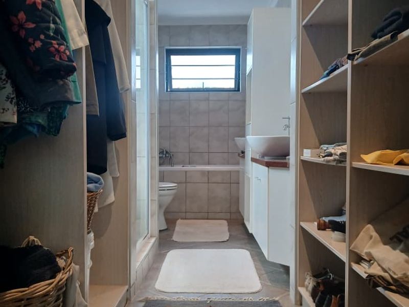 A well-organized walk-through bathroom featuring built-in cabinetry, a vessel sink, a bathtub, and a toilet, finished with neutral tiling and recessed lighting.