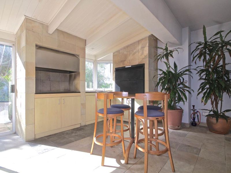 Covered patio area featuring a built-in braai, stone tile flooring, and exposed beam ceiling, perfect for outdoor entertaining.