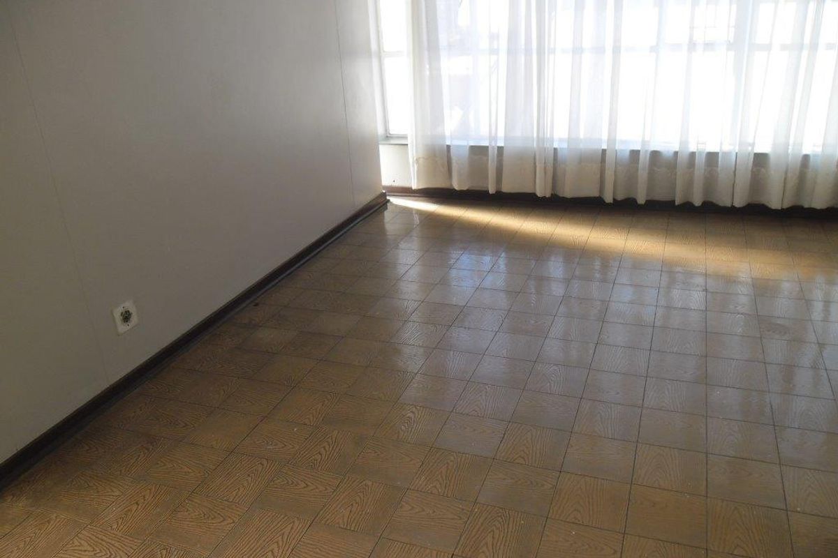 An empty living room featuring parquet flooring and large windows with sheer curtains, offering a blank canvas for interior design.