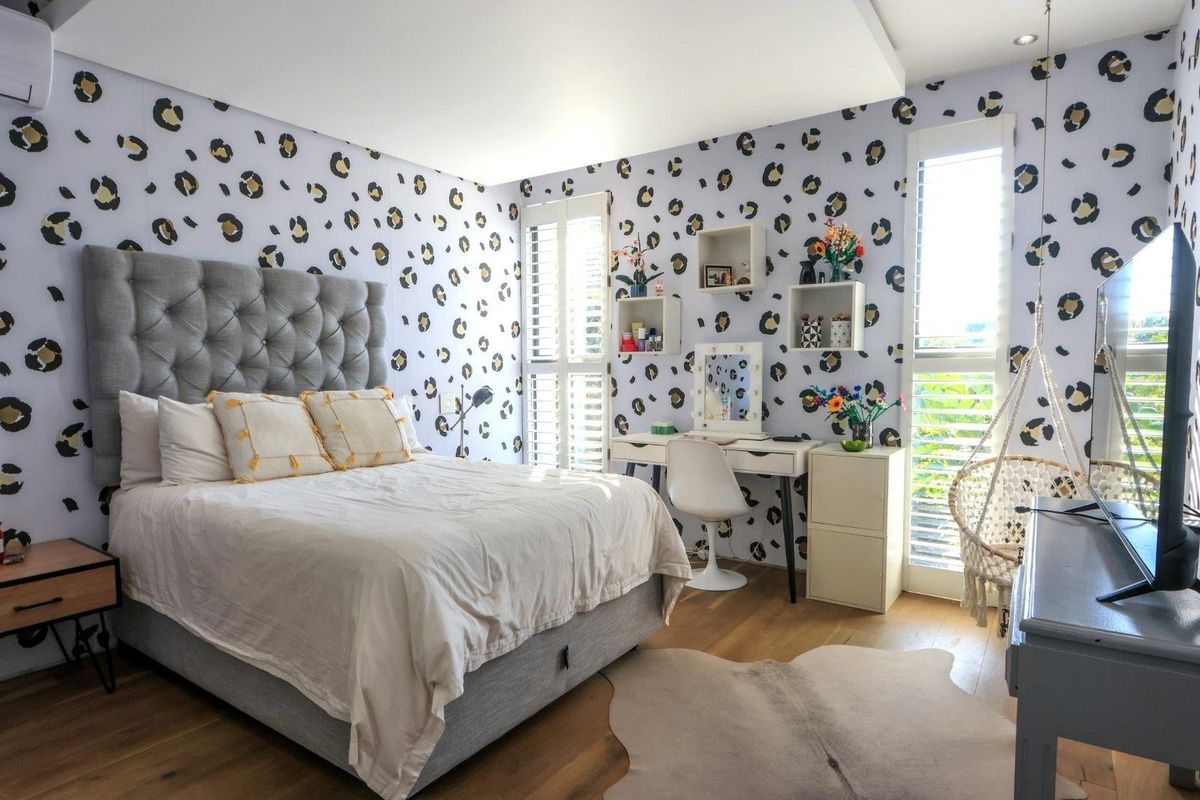 A well-maintained bedroom featuring timber flooring, plantation shutters, and a recessed ceiling, finished with distinctive patterned wallpaper.