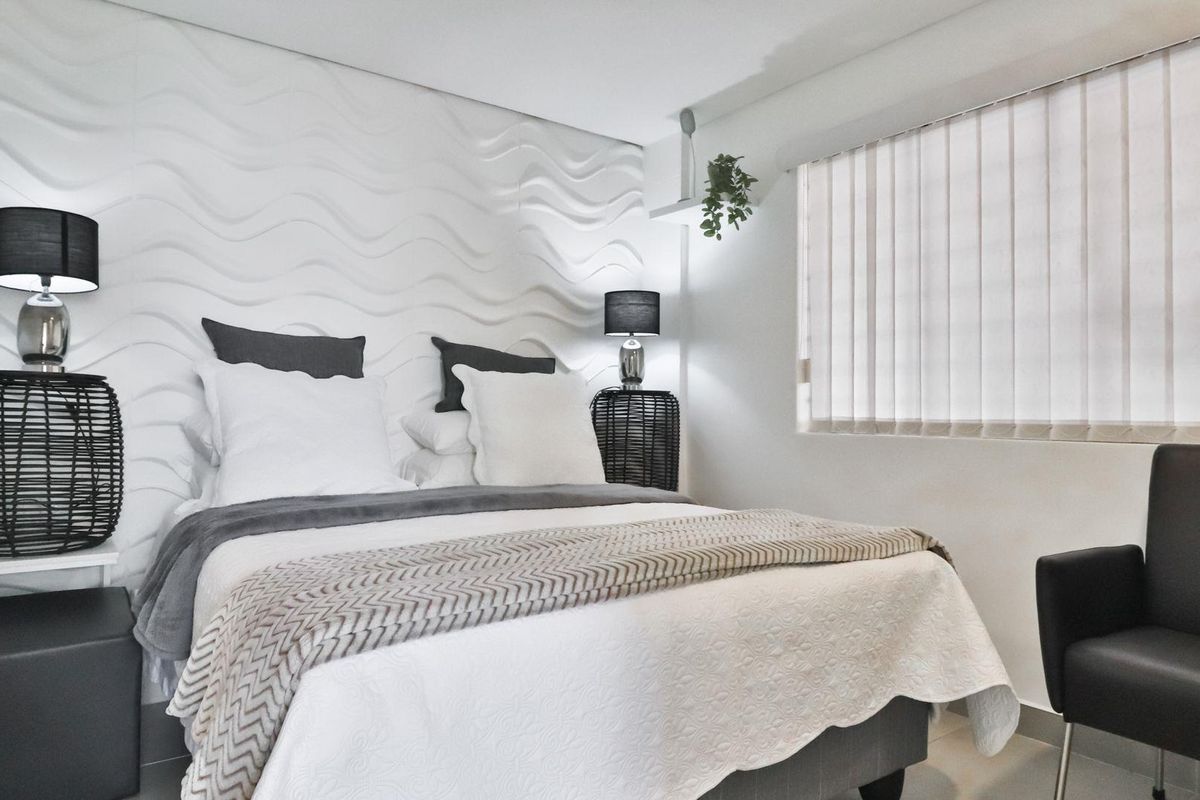 A well-maintained bedroom featuring a textured feature wall, vertical blinds, and neutral flooring.