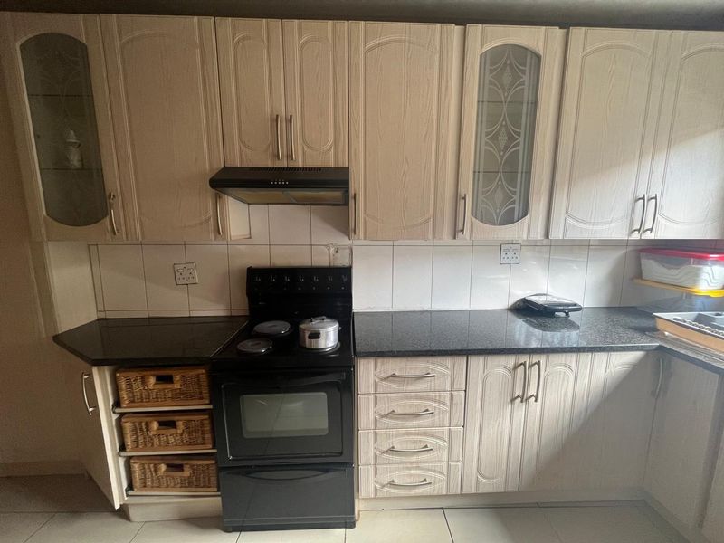 A functional kitchen featuring light-toned built-in cabinetry, dark granite countertops, a tiled backsplash, and a freestanding electric stove with an extractor fan.