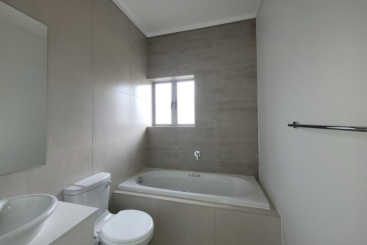 A modern, neutral-toned bathroom featuring a built-in bathtub, a vanity with a vessel sink, and tiled wall finishes.
