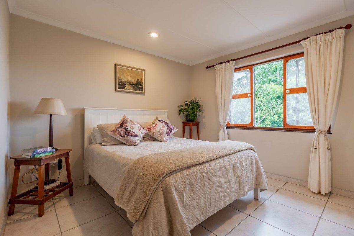 A well-lit bedroom featuring neutral wall tones, tiled flooring, and a large window with wooden frames overlooking greenery.