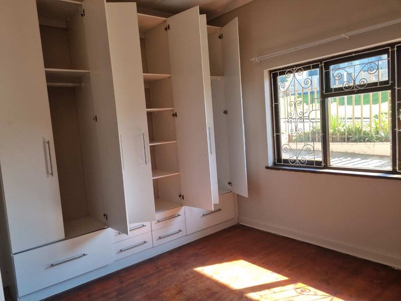 A bedroom featuring extensive built-in white cabinetry, original wooden flooring, and a window fitted with security bars.
