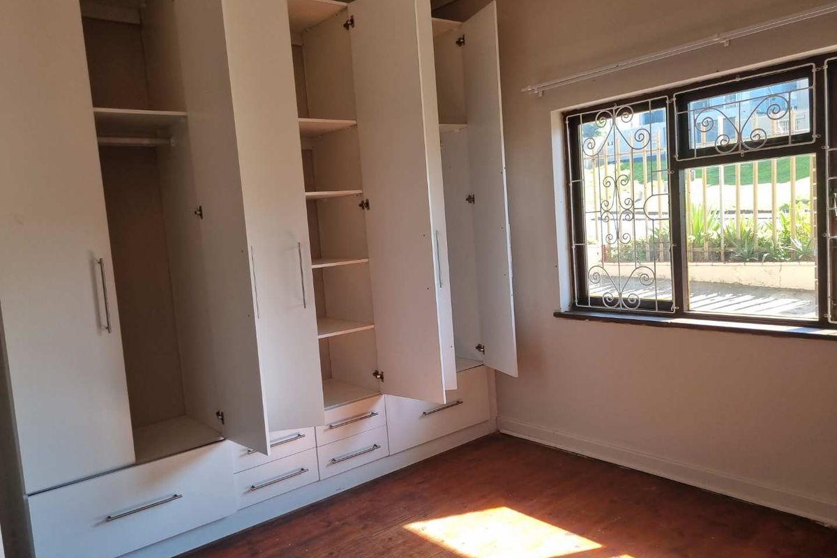 A bedroom featuring extensive built-in white cabinetry, original wooden flooring, and a window fitted with security bars.