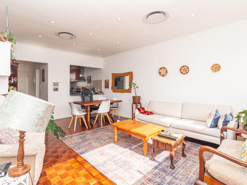 Spacious open-plan living and dining area featuring warm parquet flooring, recessed lighting, and a convenient pass-through window connecting to the kitchen.