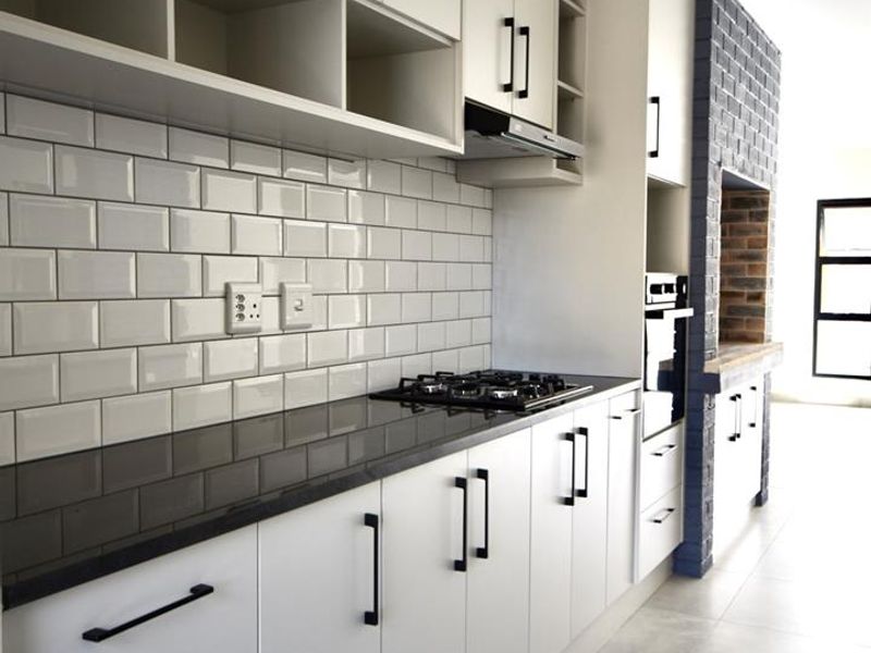 Modern kitchen featuring sleek cabinetry, subway tile backsplash, stone countertops, gas hob, and a distinctive brick feature wall with built-in oven.