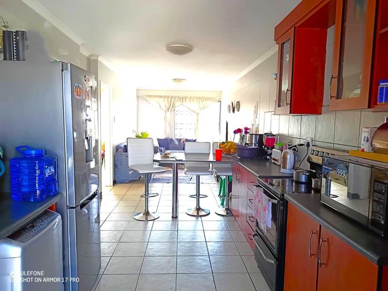 Open-plan kitchen and living area featuring tiled flooring, wooden cabinetry, and a functional layout connecting the cooking space to the lounge.