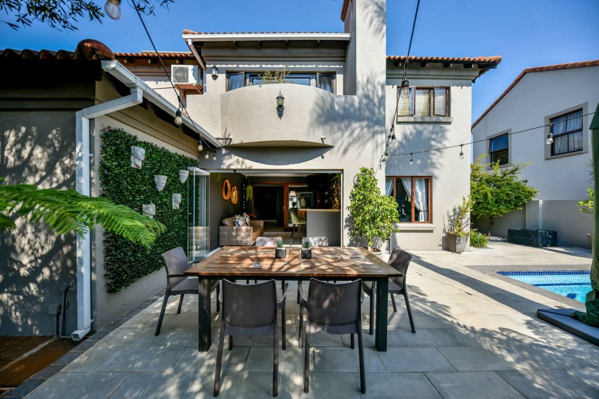 Rear exterior view featuring a paved patio area, swimming pool, and a two-story house facade with a balcony and chimney.