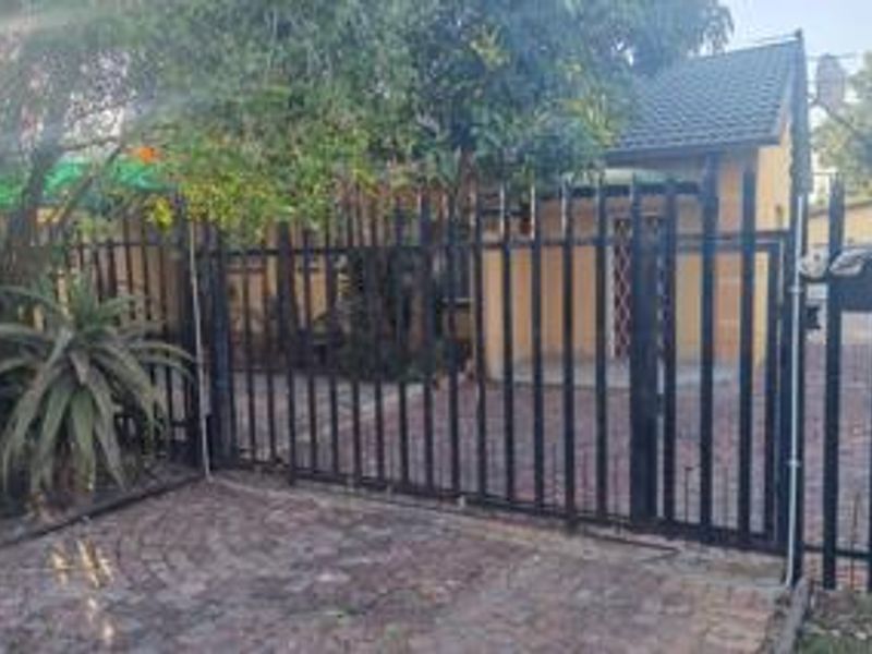 Front view of the property featuring a paved driveway, secure metal fencing, and a tiled roof structure.