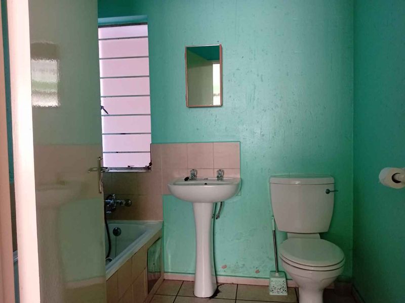 A functional bathroom featuring a pedestal basin, toilet, and bathtub with tiled splashbacks and louvered window, requiring cosmetic updates to the wall finishes.