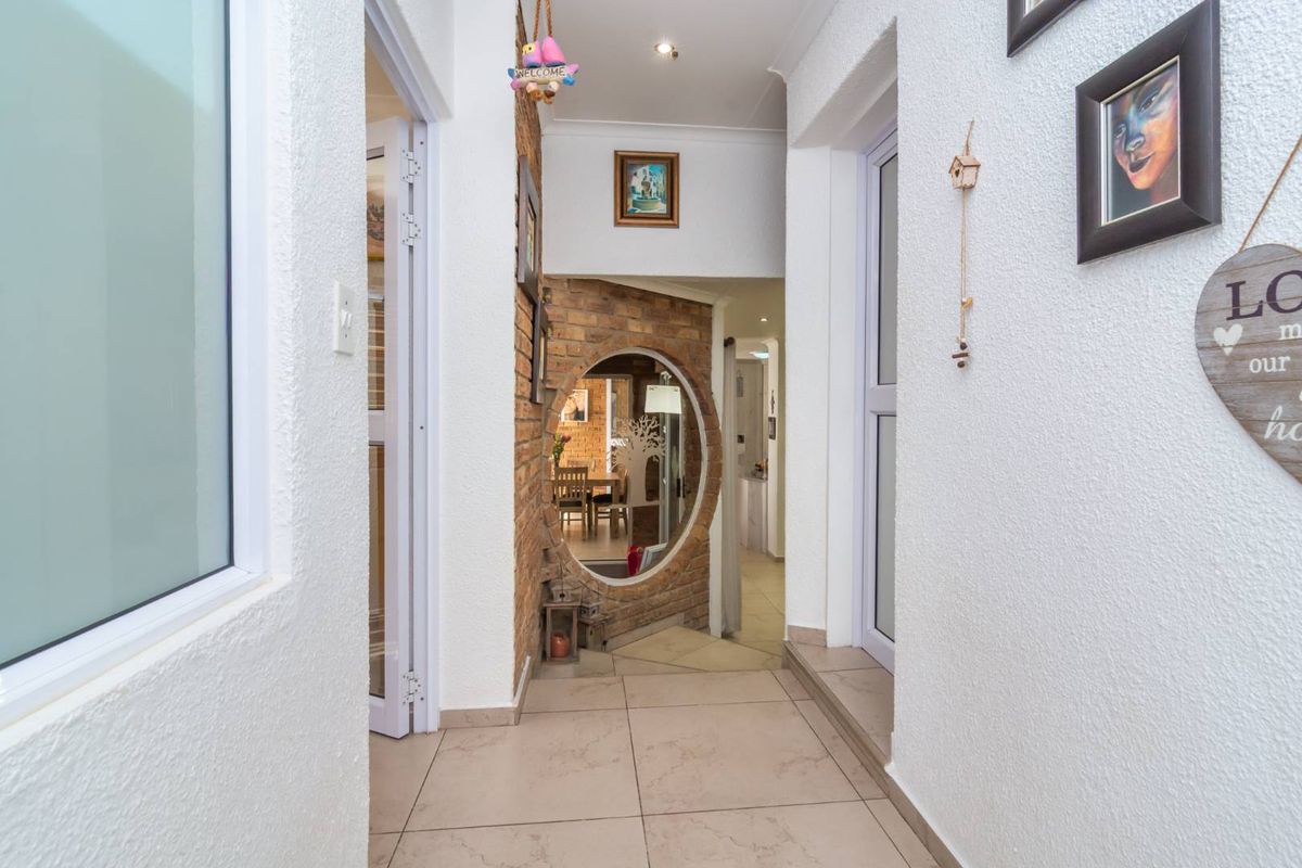 A bright hallway featuring tiled flooring, recessed lighting, and a unique circular window set into an exposed brick feature wall.