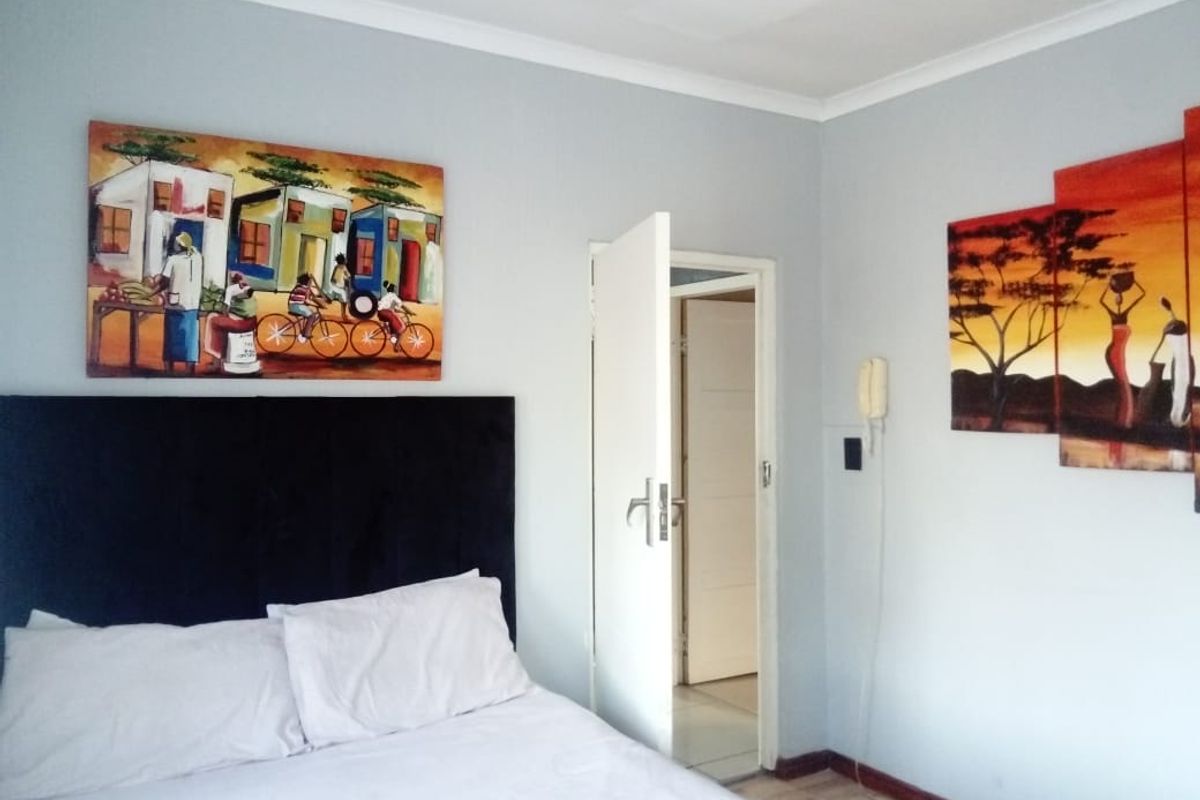 A bedroom featuring light grey walls, laminate flooring, and a doorway leading to an adjacent room.