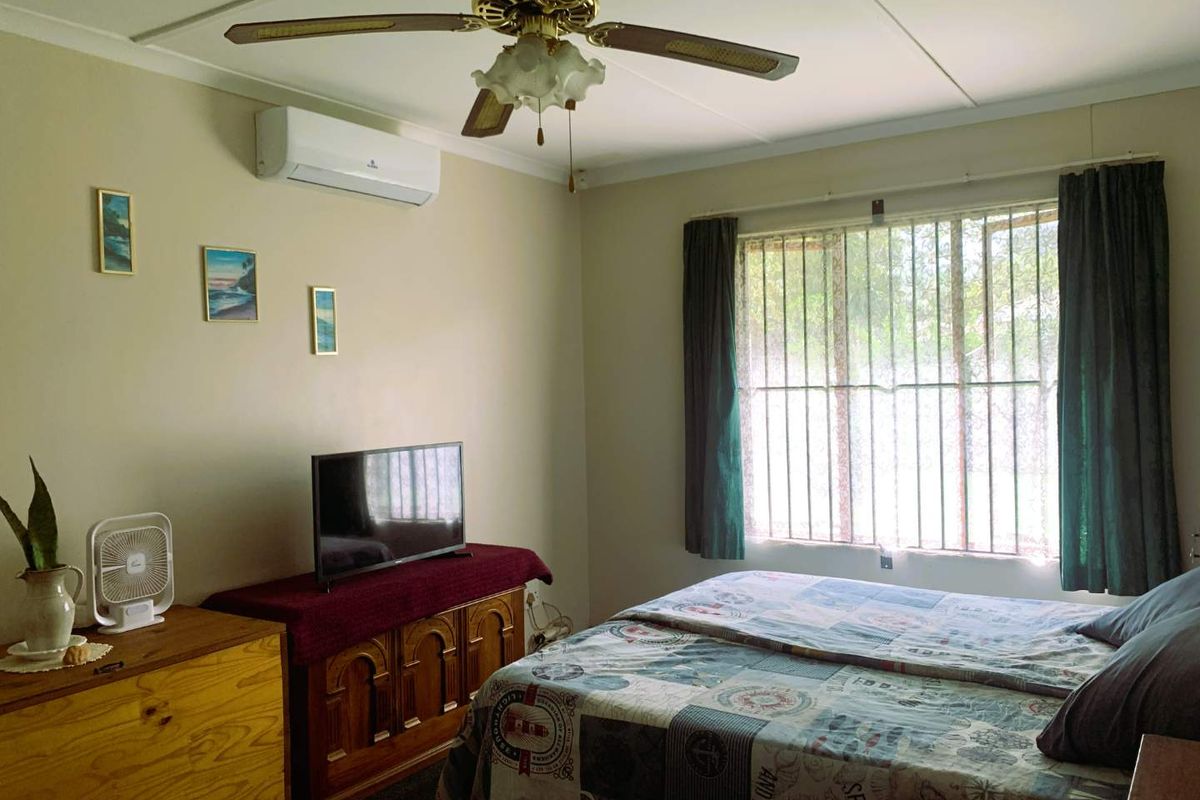 A functional bedroom featuring a ceiling fan, wall-mounted air conditioning unit, and security bars on the window.