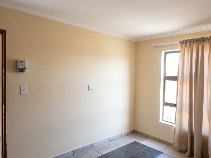 A clean, empty bedroom featuring neutral wall tones, tiled flooring, and an aluminium-framed window, providing a versatile space ready for personalization.