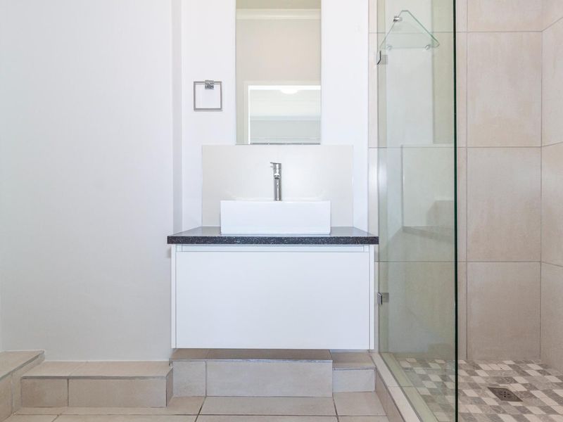Modern bathroom featuring a floating vanity with a vessel sink, chrome fixtures, and a glass-enclosed shower with tiled flooring.