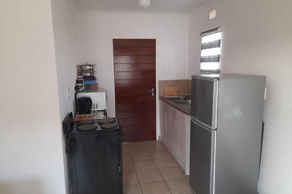 Compact kitchen featuring tiled flooring, built-in cabinetry, stainless steel sink, and space for a freestanding stove and refrigerator.