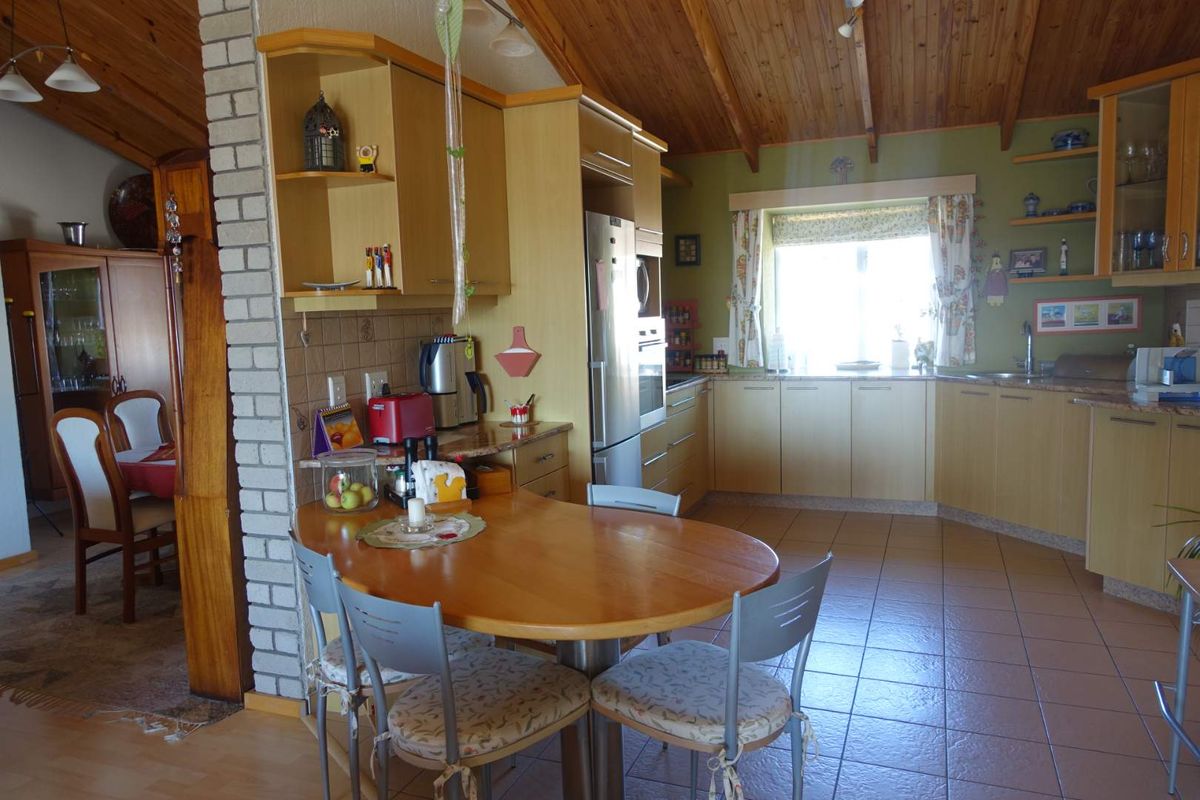 A functional kitchen featuring light wood cabinetry, tiled flooring, and a vaulted timber ceiling, with an integrated dining area.