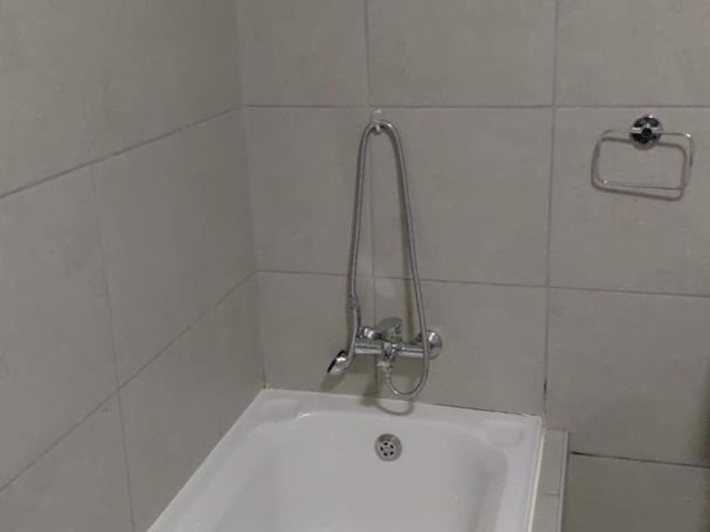 A functional bathroom featuring a white bathtub with a wall-mounted shower mixer and neutral tiled wall finishes.