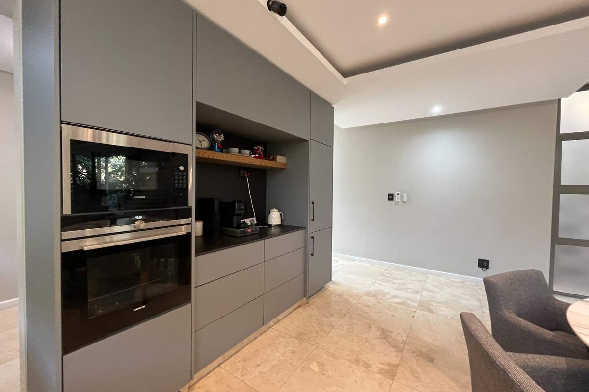 Modern kitchen featuring sleek grey cabinetry, integrated Siemens oven and microwave, recessed ceiling lighting, and neutral stone floor tiles.